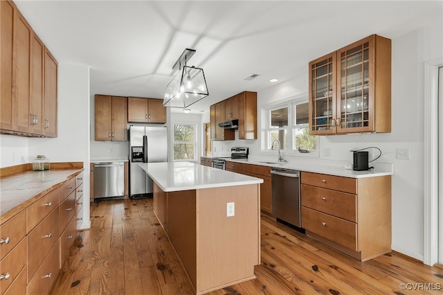 kitchen featuring a center island, appliances with stainless steel finishes, a sink, brown cabinets, and wood-type flooring