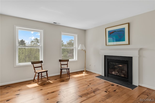 living area with visible vents, baseboards, light wood-type flooring, and a glass covered fireplace