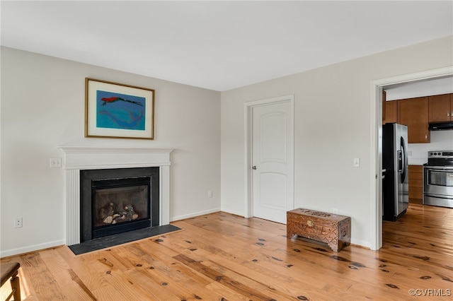 unfurnished living room with a fireplace with flush hearth, baseboards, and light wood finished floors