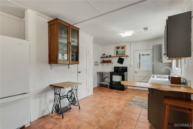 kitchen with visible vents, freestanding refrigerator, glass insert cabinets, black / electric stove, and light countertops