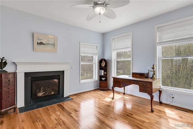 living area featuring light wood-style floors, a fireplace with flush hearth, a ceiling fan, visible vents, and baseboards