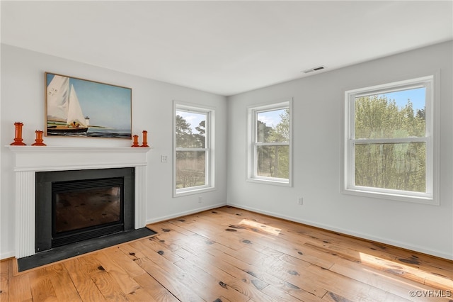 unfurnished living room with a fireplace with flush hearth, a wealth of natural light, visible vents, and hardwood / wood-style flooring