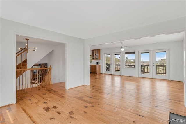 unfurnished living room with french doors, light wood-type flooring, and ceiling fan with notable chandelier
