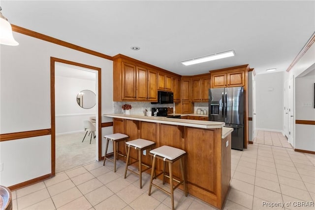 kitchen featuring brown cabinetry, light tile patterned floors, light countertops, and black appliances