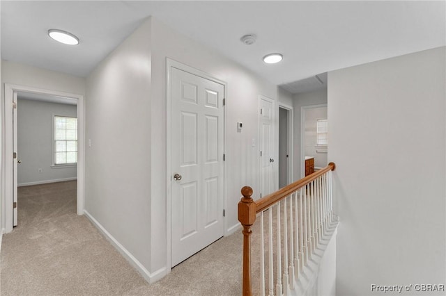 corridor with baseboards, an upstairs landing, and light colored carpet