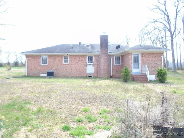 back of property featuring brick siding, cooling unit, a chimney, and a lawn
