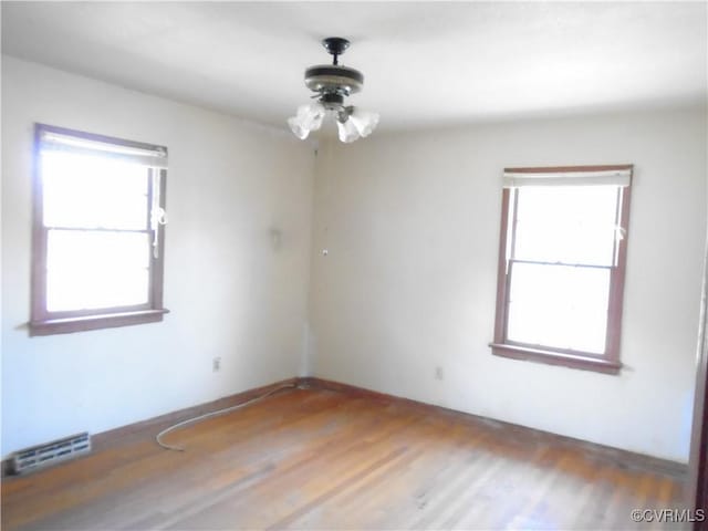 unfurnished room with a healthy amount of sunlight, wood finished floors, and visible vents