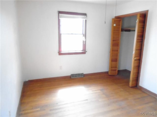 unfurnished bedroom with wood finished floors, a closet, and visible vents