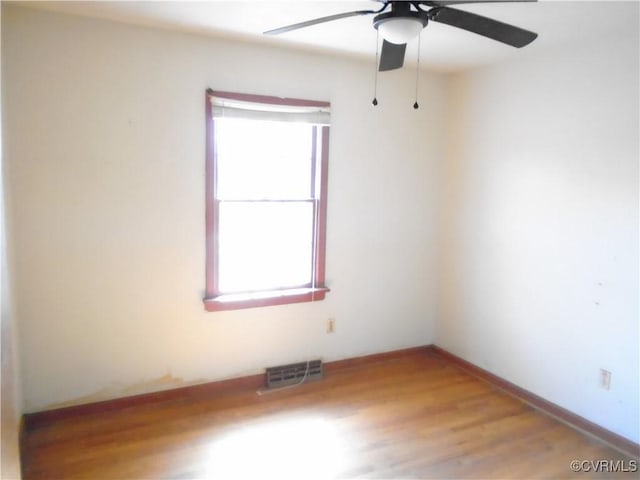 spare room with plenty of natural light, visible vents, wood finished floors, and ceiling fan