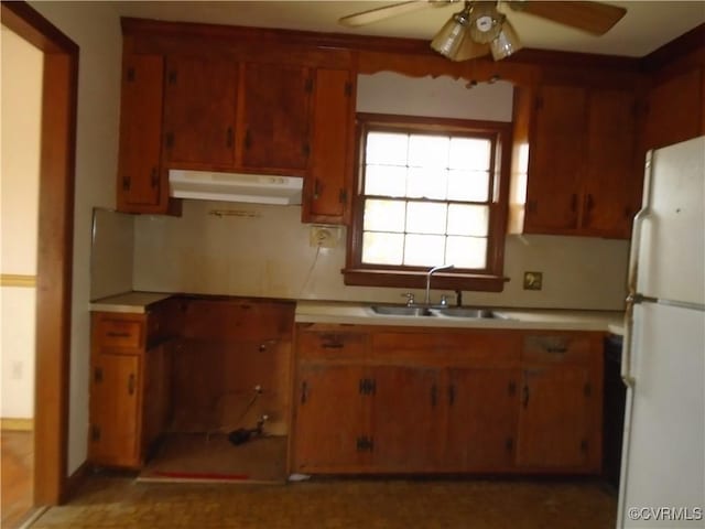 kitchen featuring a sink, ceiling fan, freestanding refrigerator, under cabinet range hood, and brown cabinets