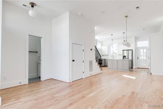 unfurnished living room featuring stairs, light wood finished floors, visible vents, and a sink