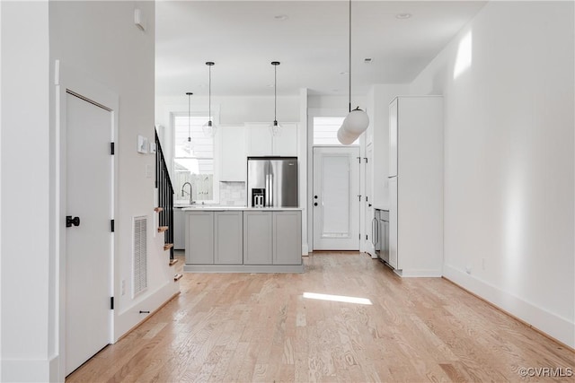 kitchen with light wood-type flooring, light countertops, stainless steel refrigerator with ice dispenser, decorative light fixtures, and visible vents