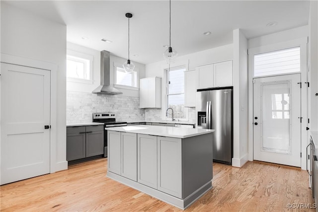 kitchen with wall chimney range hood, gray cabinets, a center island, appliances with stainless steel finishes, and backsplash