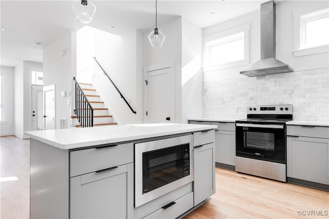 kitchen featuring wall chimney exhaust hood, electric range, gray cabinets, light countertops, and built in microwave