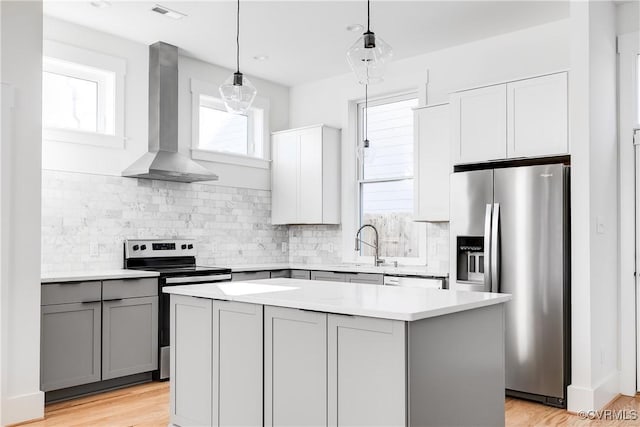 kitchen with wall chimney range hood, light countertops, gray cabinetry, stainless steel appliances, and a kitchen island