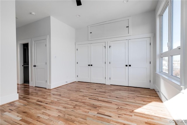 unfurnished bedroom featuring light wood-style floors, baseboards, and multiple closets
