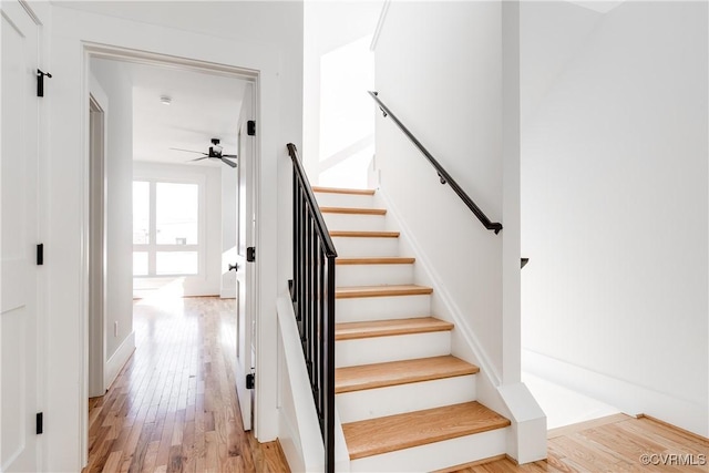 stairway with wood finished floors and a ceiling fan