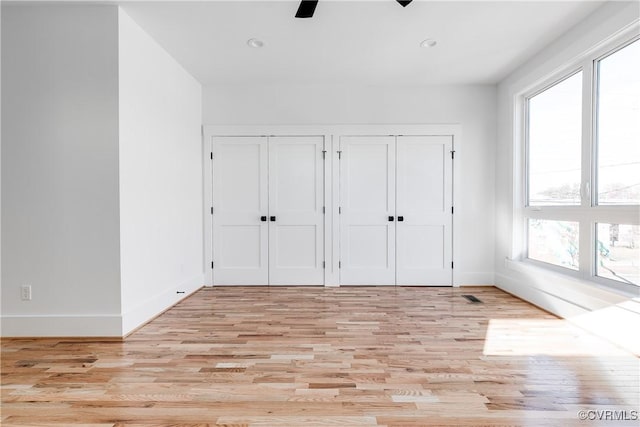 unfurnished bedroom with light wood-type flooring, multiple closets, multiple windows, and baseboards