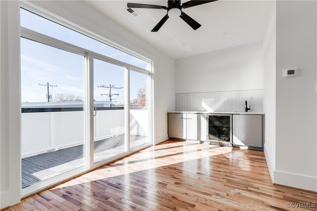 unfurnished living room featuring light wood-type flooring, visible vents, beverage cooler, and ceiling fan
