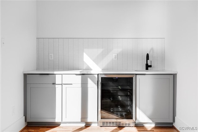 bar featuring indoor wet bar, a sink, beverage cooler, light wood finished floors, and backsplash