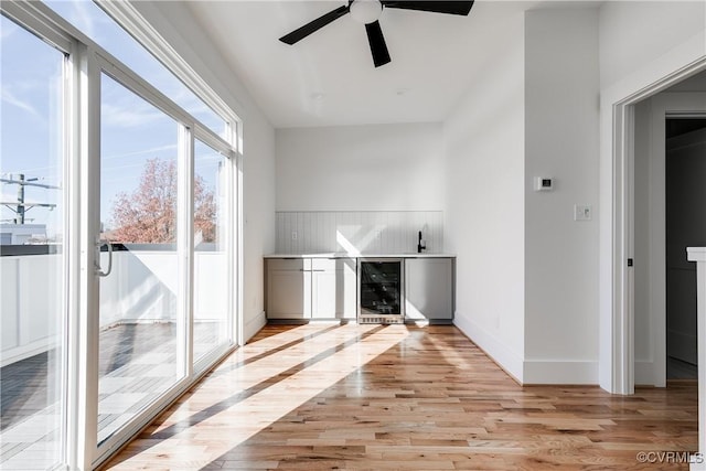 unfurnished living room with wine cooler, ceiling fan, light wood finished floors, and baseboards