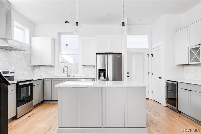 kitchen featuring wall chimney range hood, stainless steel refrigerator with ice dispenser, wine cooler, electric stove, and a sink