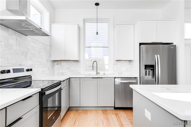 kitchen with a sink, wall chimney range hood, a wealth of natural light, and stainless steel appliances