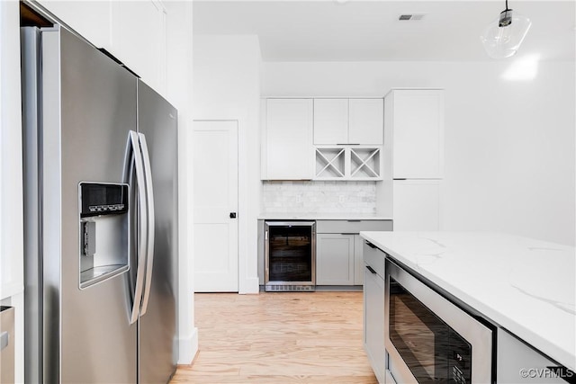 kitchen with stainless steel refrigerator with ice dispenser, beverage cooler, light stone counters, and decorative backsplash