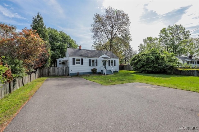 view of front of house featuring fence, a chimney, a front lawn, and aphalt driveway