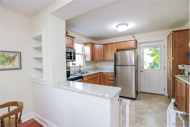 kitchen with brown cabinets, appliances with stainless steel finishes, a sink, light countertops, and a peninsula