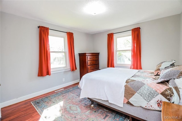 bedroom featuring visible vents, baseboards, wood finished floors, and multiple windows