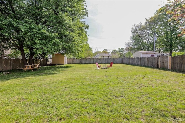 view of yard with a storage unit, a fenced backyard, and an outdoor fire pit