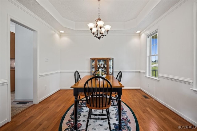 dining area featuring a chandelier, a raised ceiling, light wood-style floors, and baseboards