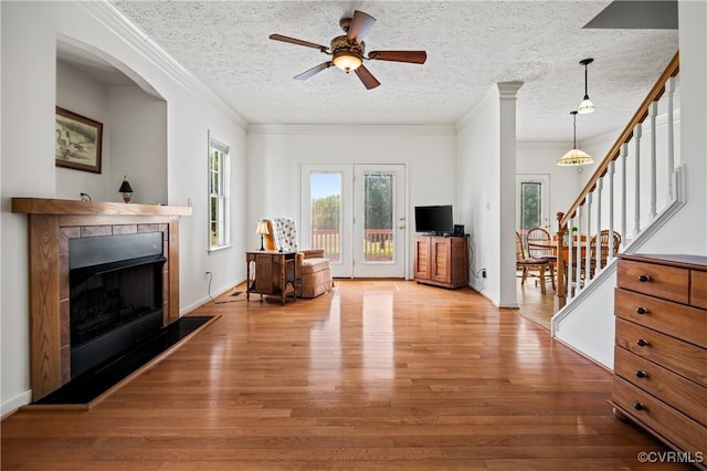 living area with wood finished floors, a fireplace with raised hearth, stairs, and ornamental molding