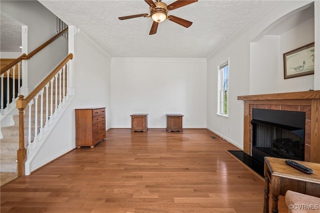 unfurnished living room featuring a fireplace with flush hearth, a ceiling fan, light wood-type flooring, a textured ceiling, and stairs