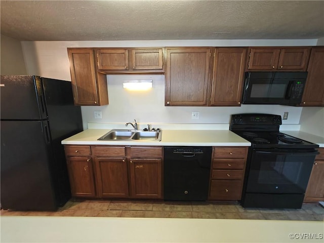 kitchen featuring light countertops, a textured ceiling, a sink, and black appliances