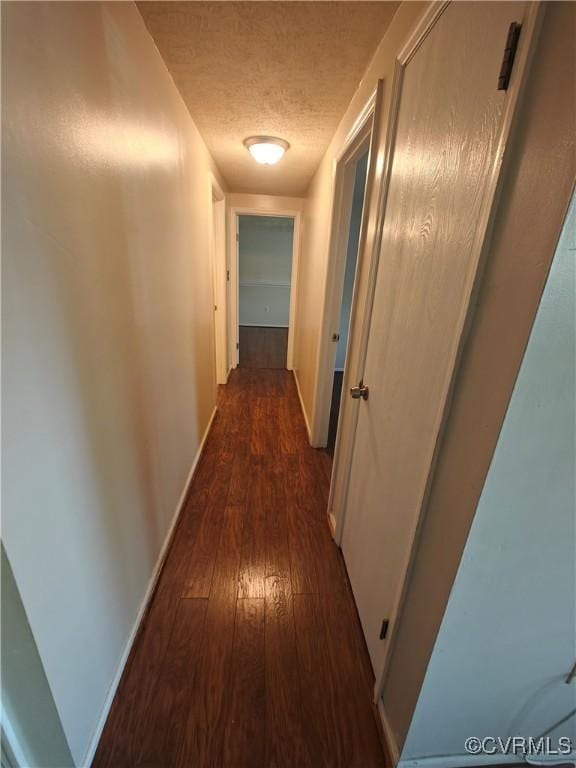 hallway featuring a textured ceiling, baseboards, and dark wood-style floors