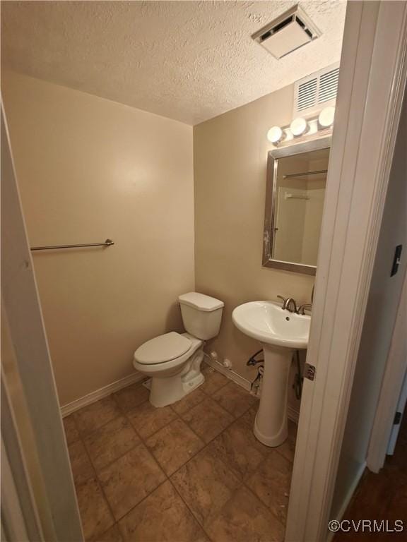 half bathroom featuring visible vents, toilet, baseboards, and a textured ceiling