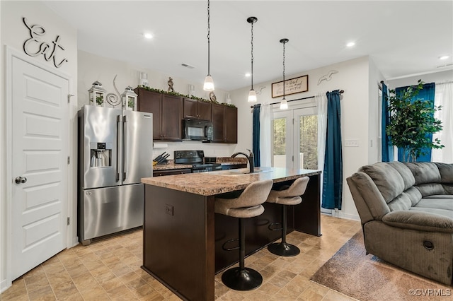 kitchen featuring open floor plan, dark brown cabinets, a center island with sink, a breakfast bar area, and black appliances