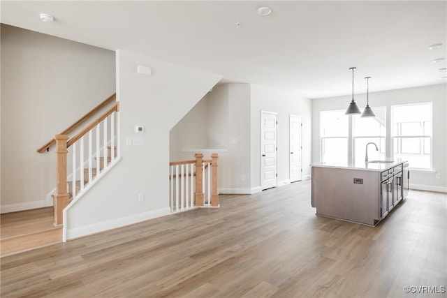 kitchen featuring baseboards, light countertops, light wood finished floors, and a sink