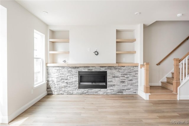 unfurnished living room with baseboards, stairway, wood finished floors, and built in features