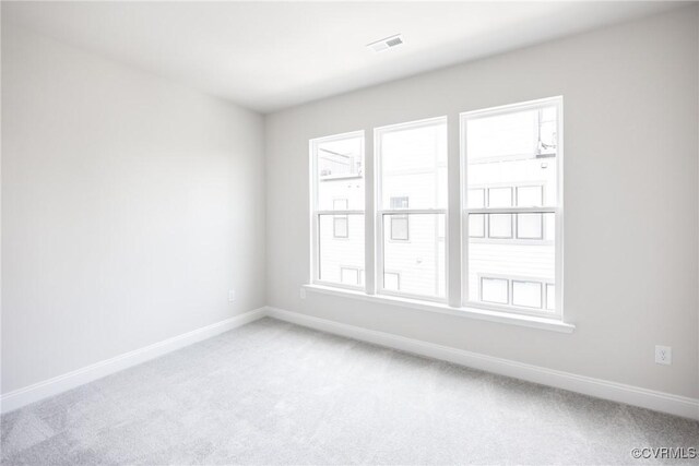 spare room featuring plenty of natural light, light carpet, and baseboards