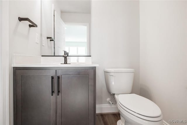 half bathroom featuring toilet, wood finished floors, vanity, and baseboards