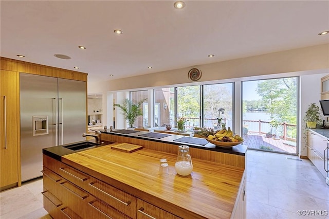 kitchen featuring a sink, butcher block countertops, brown cabinetry, recessed lighting, and stainless steel built in fridge