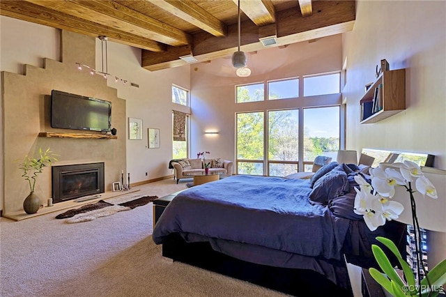 bedroom with wood ceiling, a towering ceiling, carpet floors, beamed ceiling, and a glass covered fireplace