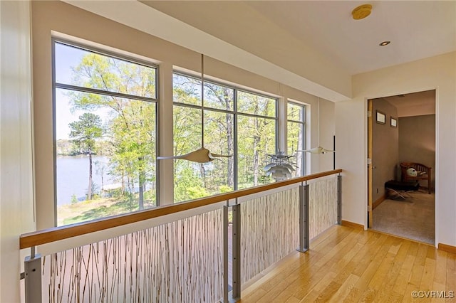 corridor with a water view, baseboards, a healthy amount of sunlight, and light wood-style floors