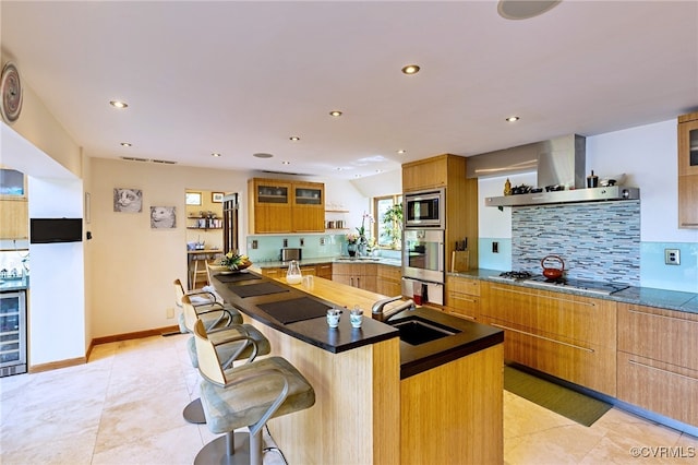 kitchen featuring a kitchen island, beverage cooler, wall chimney range hood, a sink, and appliances with stainless steel finishes