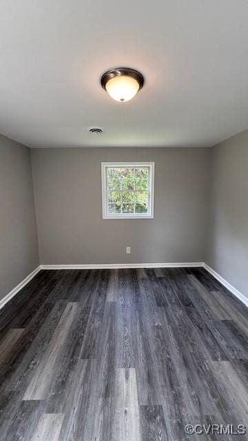 unfurnished room with visible vents, dark wood finished floors, and baseboards