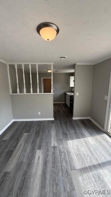 unfurnished living room featuring a textured ceiling, a sink, baseboards, and dark wood-type flooring