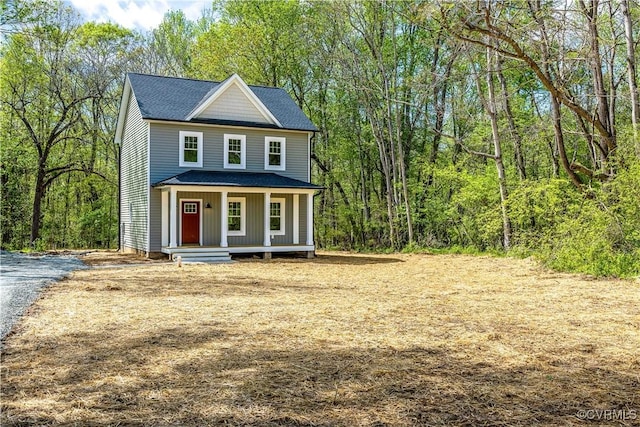 view of front of property with a porch, a shingled roof, and a forest view